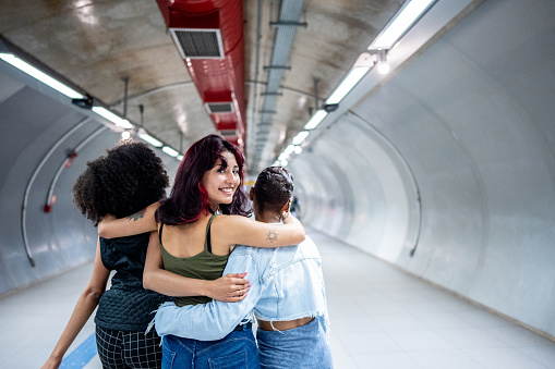 Portrait of a young woman walking while embracing her friends at the subway station