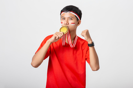 Young Indonesian man holding gold medal celebrate Indonesia independence day 17 August isolated on white background. Dirgahayu 78 Tahun Kemerdekaan Indonesia.