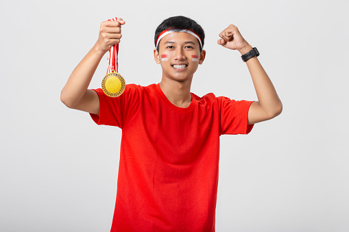 Young Indonesian man holding gold medal celebrate Indonesia independence day 17 August isolated on white background. Dirgahayu 78 Tahun Kemerdekaan Indonesia.