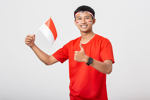 Young Indonesian man waving flag of Indonesia celebrate independence day 17 August isolated on white background. Dirgahayu 78 Tahun Kemerdekaan Indonesia.