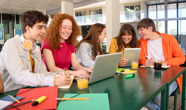 istock Smiling college classmates using laptops in campus cafeteria. Group cheerful students. 1489216768