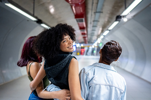 Portrait of a young woman walking while embracing her friends at the subway station