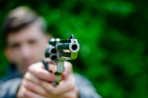 A person points a revolver in the direction of the photographer