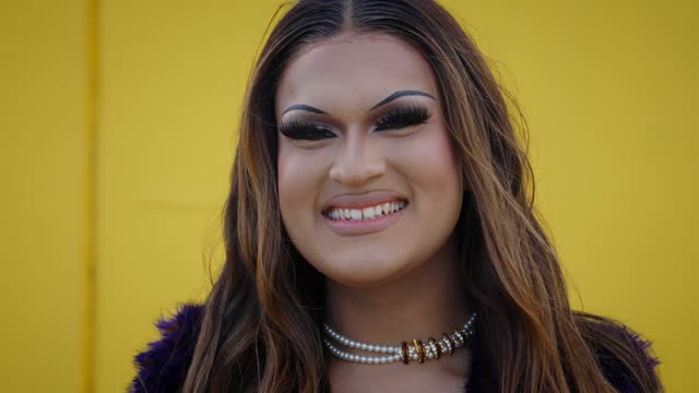 Portrait of excited transgender young with yellow background. Fun Drag Queen posing for photo.