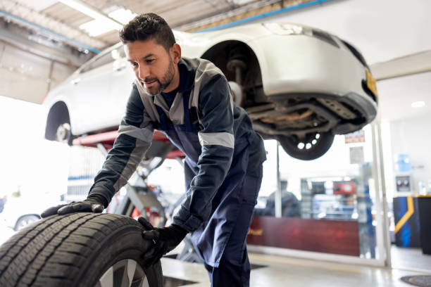 meccanico felice che cambia una gomma a terra su un'auto - auto repair shop tire car mechanic foto e immagini stock