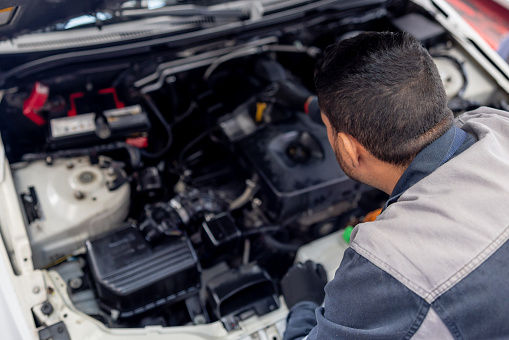 Mechanic checking the oil levels of a car under the hood at an Auto Repair Shop