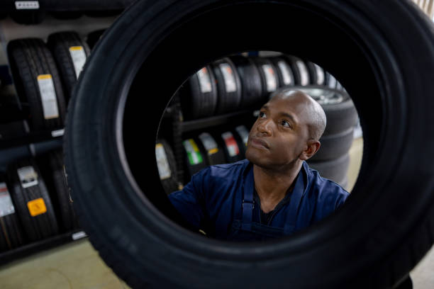 mécanicien choisissant un pneu à remplacer sur une voiture alors qu’il travaille dans un atelier de réparation automobile - usine-de-fabrication-de-pneus photos et images de collection