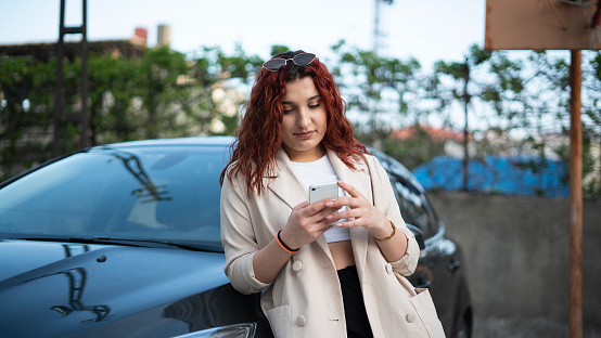 Smiling young business woman using phone near car