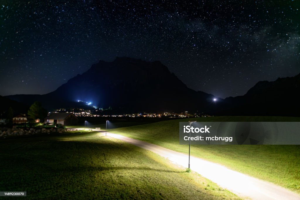 Illuminated footpath in front of the Zugspitze at night Nachtaufnahme: beleuchteter Fußweg nach Ehrwald vor der Zugspitze unter dem Sternenhimmel Night Stock Photo