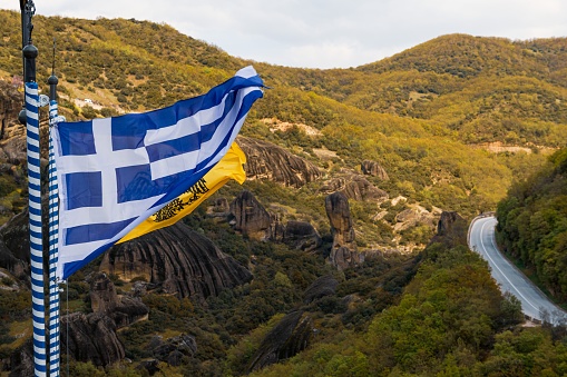 The Greek flag billowing in the breeze against a backdrop of majestic mountains. Kalabaka, Greece.