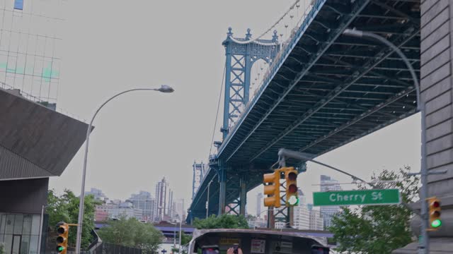 People on open desk of Hop-on Hop-of sightseeing buss passing under Brooklyn Bridge on green stoplight. New York,  USA.