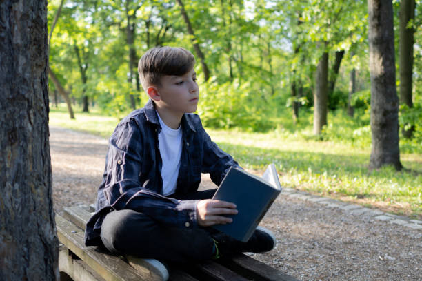 istock Schoolboy reading book in the public park 1489233476