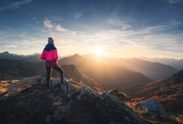 Young woman on mountain peak and beautiful mountain valley in haze at colorful sunset in autumn. Dolomites, Italy. Sporty girl, mountain ridges in fog, orange grass, trees, golden sun in fall. Hiking mujer joven en la cima de la montaña y hermoso valle de montaña en bruma en la colorida puesta de sol en otoño. dolomitas, italia. chica deportista, crestas montañosas en niebla, hierba naranja, árboles, sol dorado en otoño. excursionismo