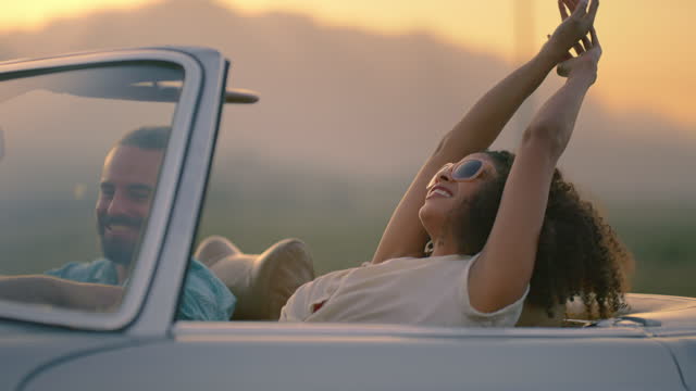 Travel, car and couple of friends with sunset on road trip, journey and freedom for summer holiday or celebration. Biracial women, partner or people with wind, hands in air and driving in convertible