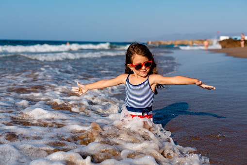 Little girl enjoys the waves by the shore on her summer holiday