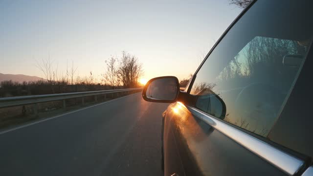 Profile of young handsome man seen in car mirror drives at sunset