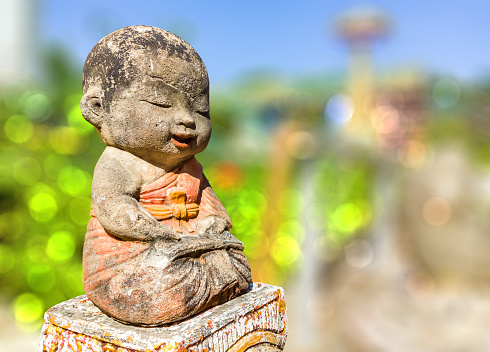 Buddhist monk statue in nature background, Close-up. Selective focus. Statue of kid monk at temple. Novice statue isolated.