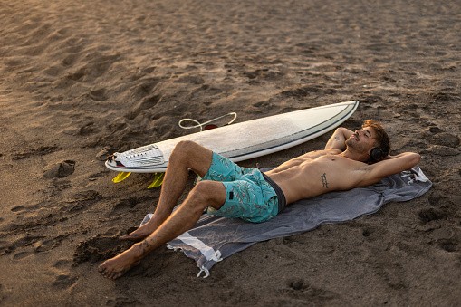 The photo conveys a sense of peace and tranquility as the surfer soaks up the beauty of the setting sun after a day of riding the waves.