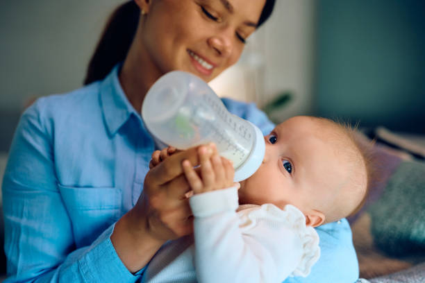 istock Baby drinking milk from a bottle while mother is holding her at home. 1489251433
