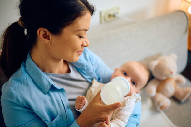 istock Smiling mother using baby bottle while feeding her daughter at home. 1489253212