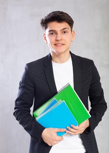 Smiling young guy teenager in business clothes with stack of notebooks in his hands