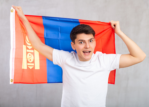 Chinese man smiling and raising a spanish national flag in studio with yellow background