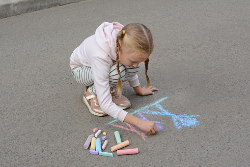 the cute little girl drawing the picture on the floor. Drawing triangle, rainbow,sun.