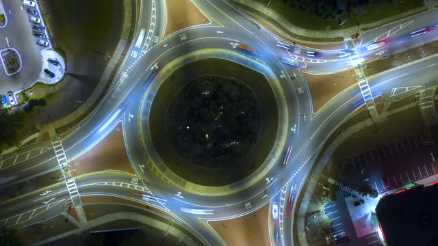 Top view of city street traffic on roundabout intersection at night with fast moving cars. Timelapse of illuminated urban circular transportation crossroads