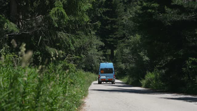 Blue van driving on evergreen forest mountain road while traveling on summer vacation, slow motion cinematic shot