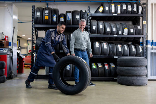 mécanicien changeant un pneu de voiture et parlant à son client au garage de réparation - auto repair shop customer auto mechanic mechanic photos et images de collection