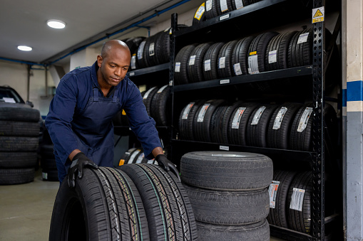 African American mechanic working at a repair garage and moving some tires