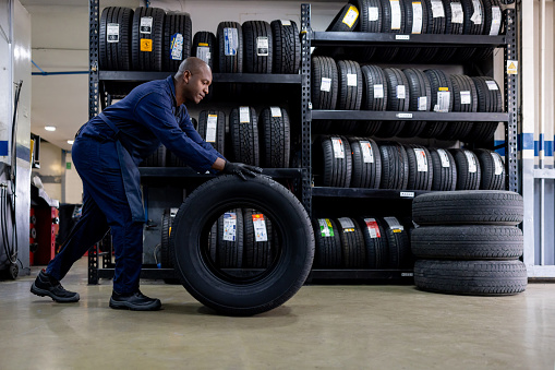 African American mechanic changing a flat tire and carrying a wheel at a repair garage