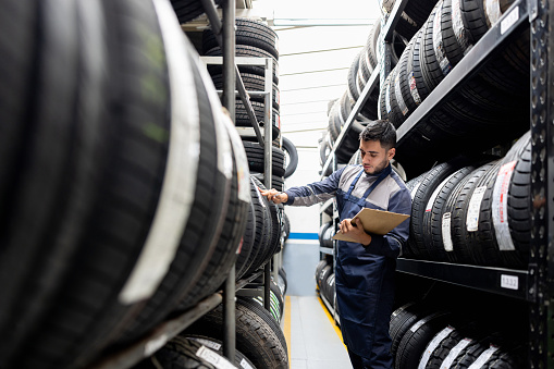 Latin American man doing a stock inventory while working at a tire factory and taking notes on a clipboard