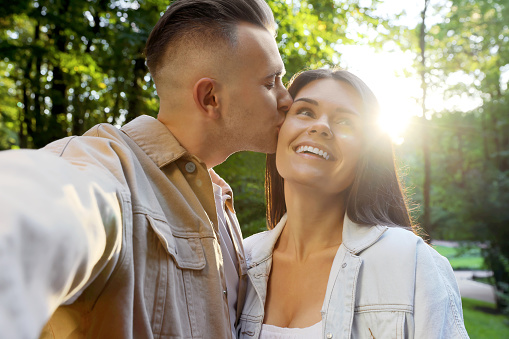 Affectionate young couple kissing and taking selfie in park