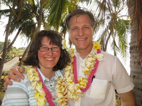 a middle aged Caucasian couple with leis in a tropical setting