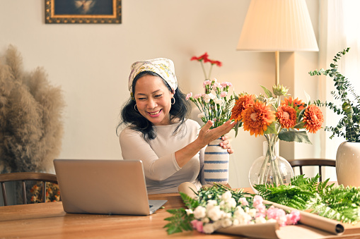 Happy and attractive mature Asian woman enjoying with her online flower arrangement workshop at home.