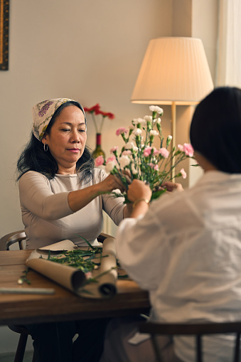 Portrait of a beautiful retired Asian woman focuses on arranging a vase with fresh flowers in a workshop. Lifestyle concept