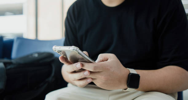 Chatbot gpt concept, asian man sitting down while looking at his smartphone, Humanizing digital experiences.