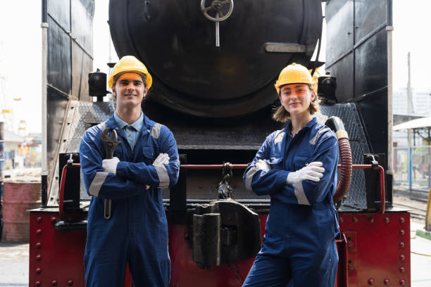 Portrait of male and female engineer worker working, standing with crossed arms, wearing safety uniform, helmet, gloves in locomotive garage. Group of railway engineer repair railhead engine in garage retrato de un ingeniero y una ingeniera trabajadora trabajando, de pie con los brazos cruzados, vistiendo uniforme de seguridad, casco, guantes en el garaje de locomotoras. grupo de ingenieros ferroviarios de reparación de motores de cabeza de carril en g