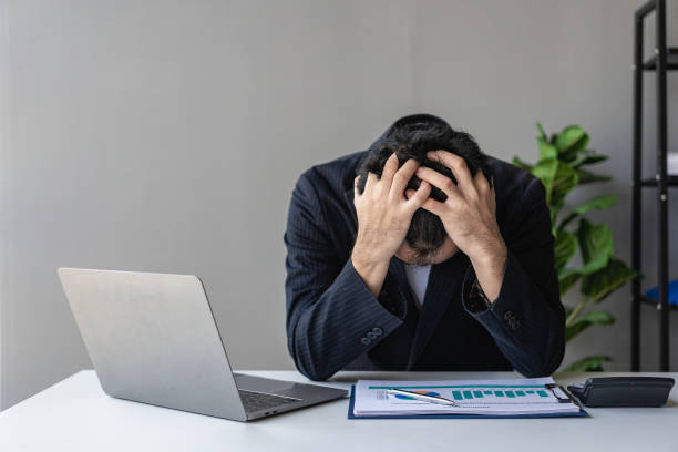 istock Young Asian businessman working on his laptop while having headache and anxiety at work while battling exhausted stress with financial documents in office. 1489320230