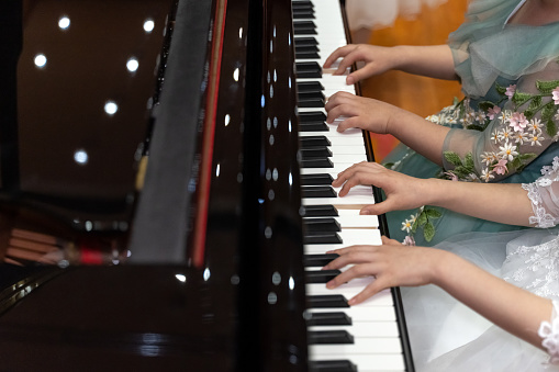 Hands of two people playing the piano together