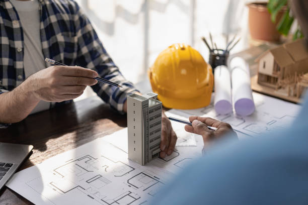 istock Engineer team meeting and talking using laptop Blueprints and papers on table with yellow hat house model in office, project manager discussing meeting with colleague 1489325135