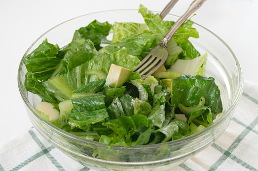 Lettuce salad with fresh avocado, and celery, and lemon olive oil dressing, close-up in a glass bowl on white background