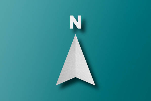 White paper cut in north arrow shape set on green paper background.