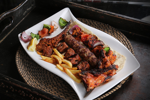 Mix grill with lamb chop, chicken tikka, shish tawook, beef kabab, fries and salad served in dish isolated on red mat top view on table arabic food