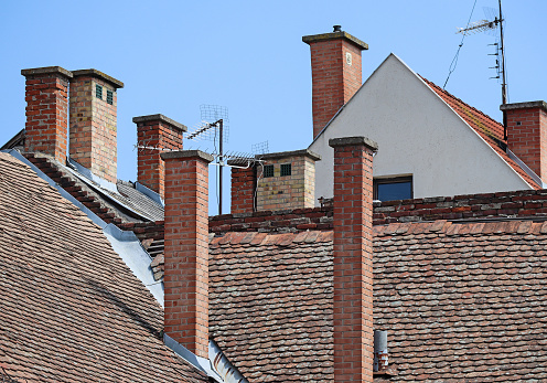 A small section of old roof tiles on a house with the chimney standing prominent
