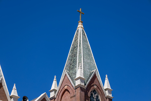 This image shows an upward view of a steeple tower on a 19th century American church in a Gothic Revival style architecture, with blue sky background.