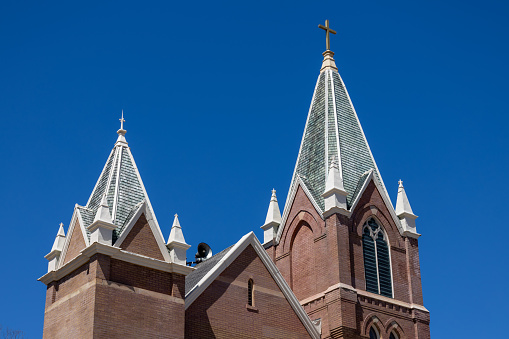This image shows an upward view of a steeple tower on a 19th century American church in a Gothic Revival style architecture, with blue sky background.