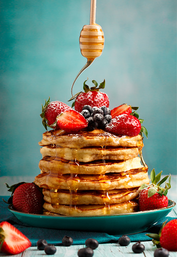 Pancakes with blueberries strawberries and honey. Aqua background. Close up