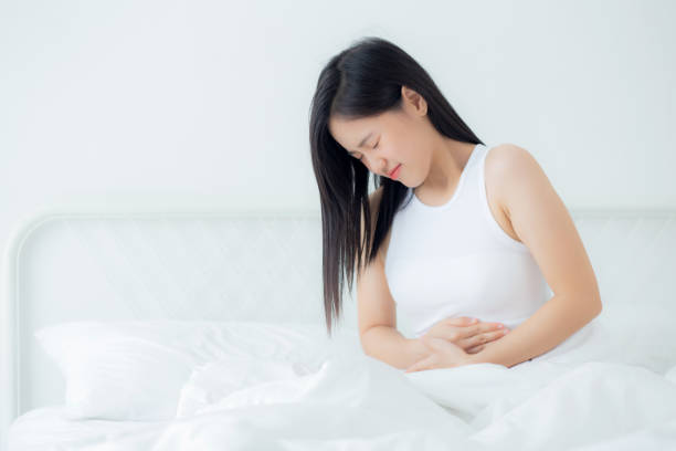 Young asian woman sitting on bed pain stomach or bowel with disease constipation in the bedroom at home, unhappy female sick and menstruation and stomachache, medical and health concept. stock photo